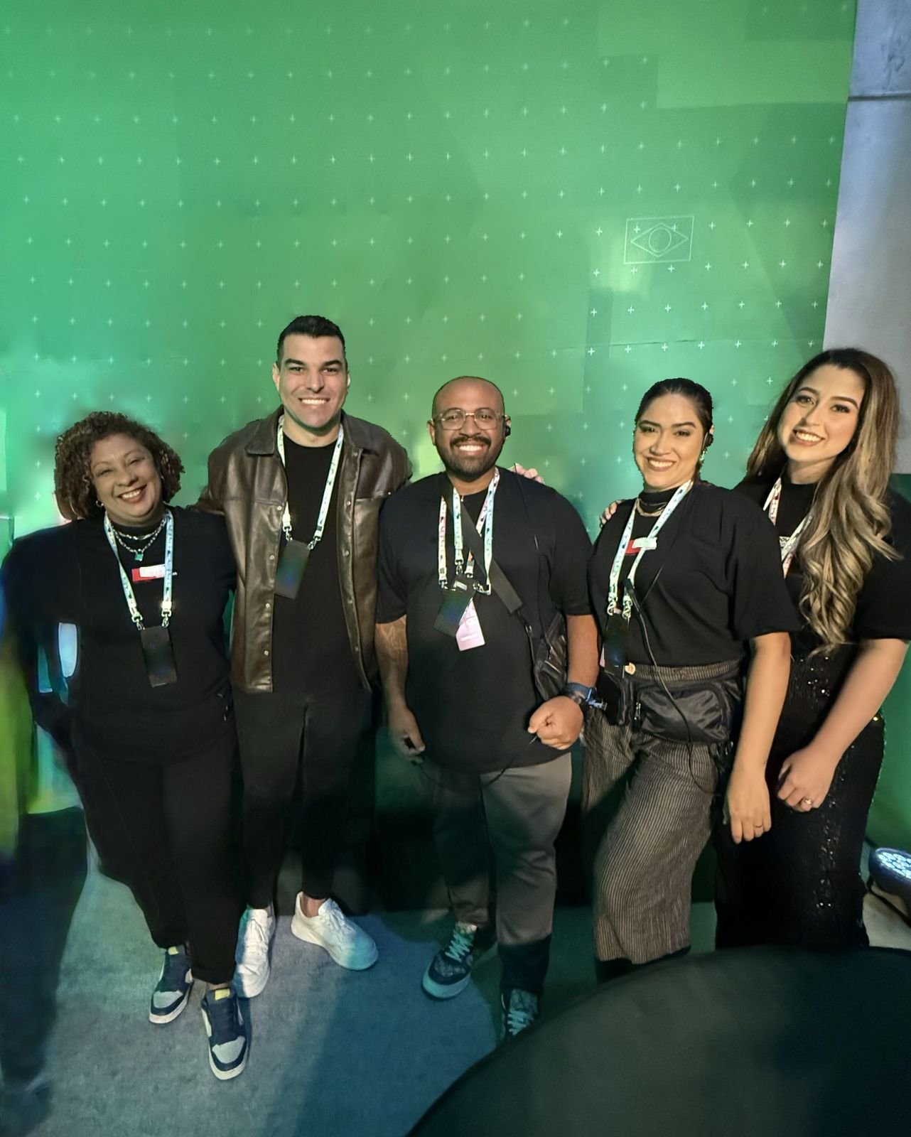 Equipe reunida diante da parede verde, com a bandeira do Brasil